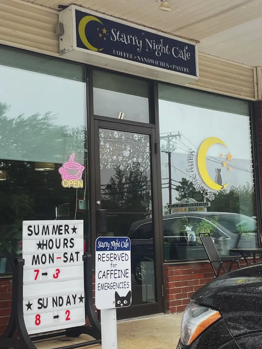 The Starry Night Cafe storefront — crescent-moon and cat sign, neon OPEN cup and the summer hours board